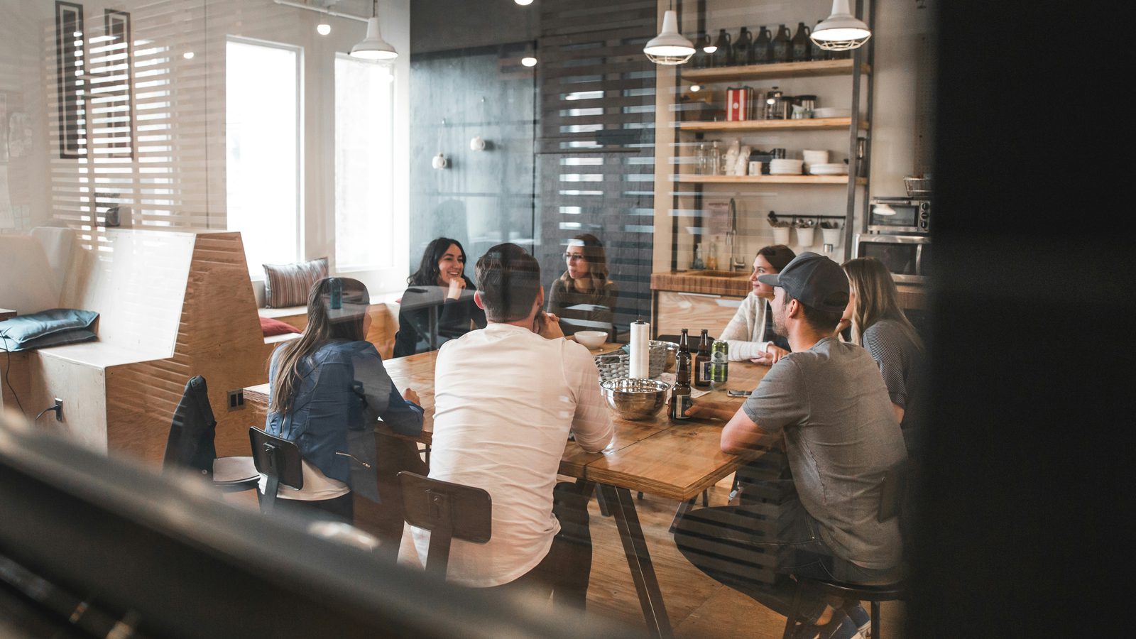Six people talking around a wooden table in a glass-walled meeting room.