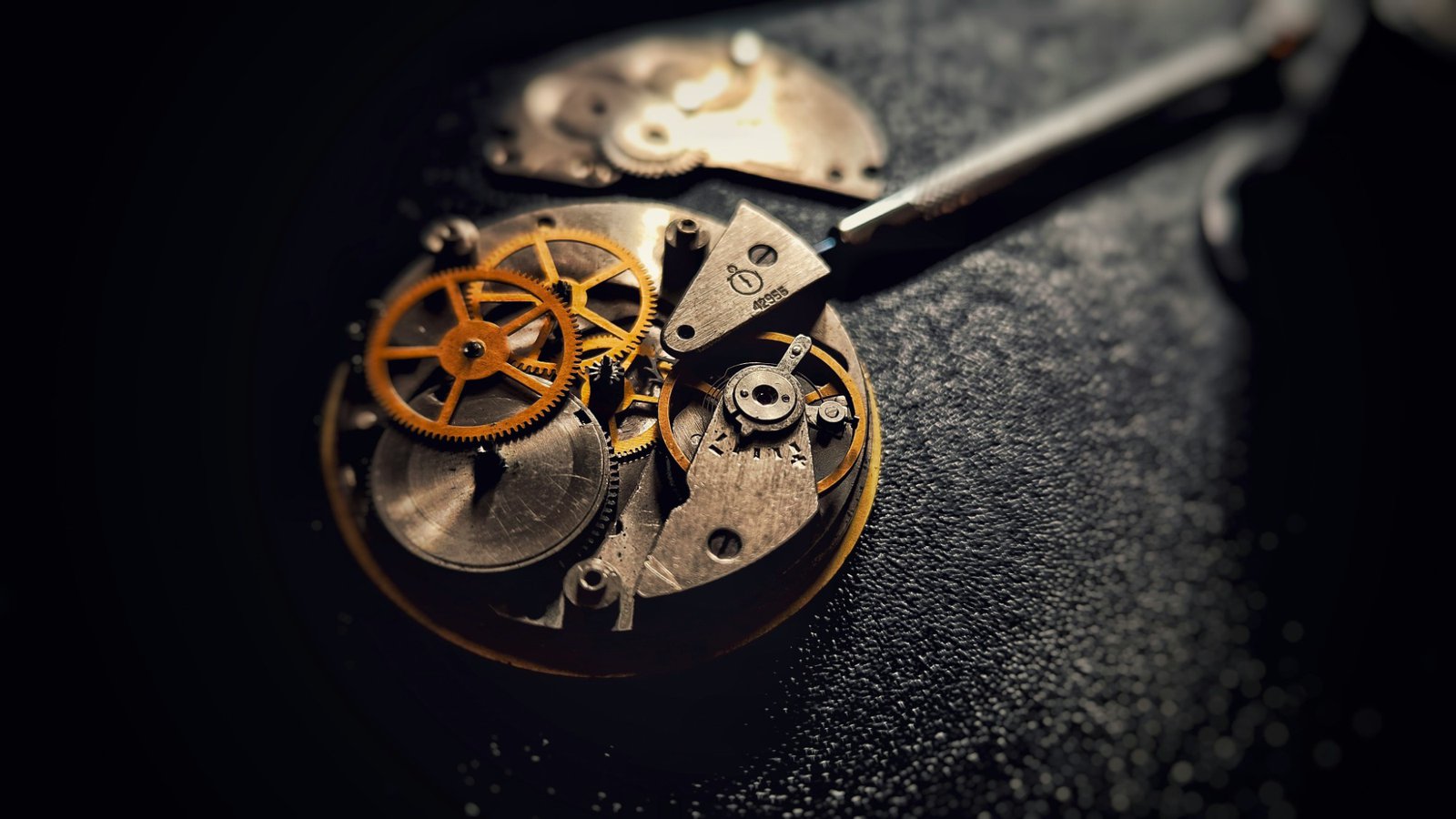 The open movement of a mechanical watch, brass gears exposed, with a screwdriver resting on the bridge.